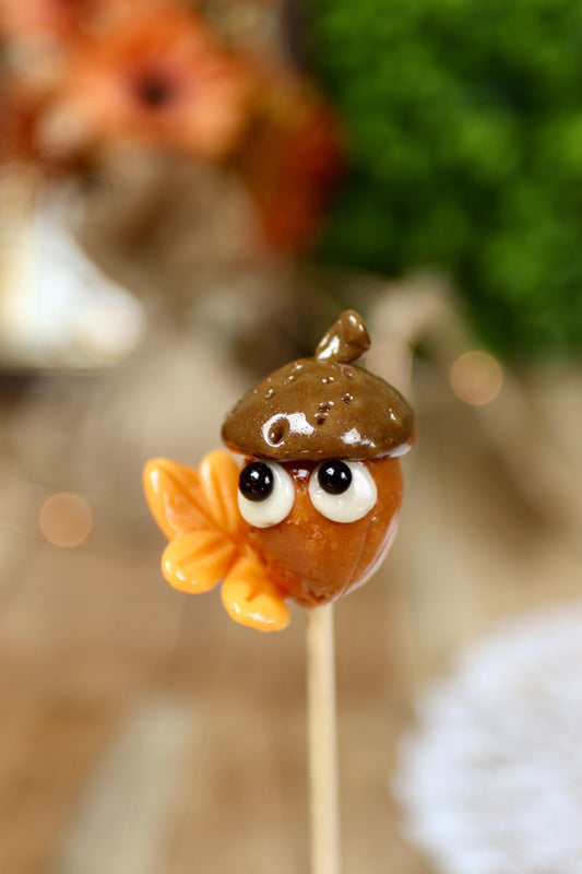 Sucette artisanale en forme de gland au caramel, avec une feuille d’automne sculptée à la main dans une teinte orange chaude.