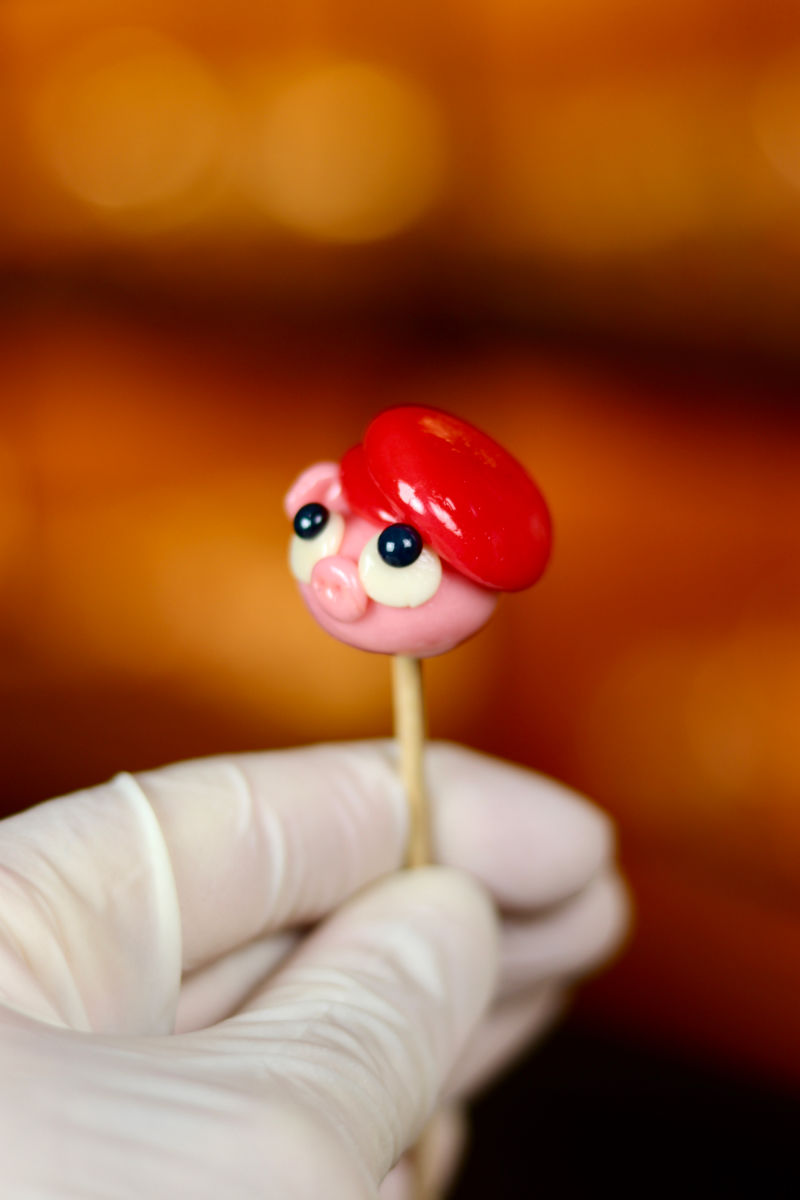 Une sucette sculptée en forme de cochon portant un béret rouge à la fraise. Photo prise dans notre boutique magique
