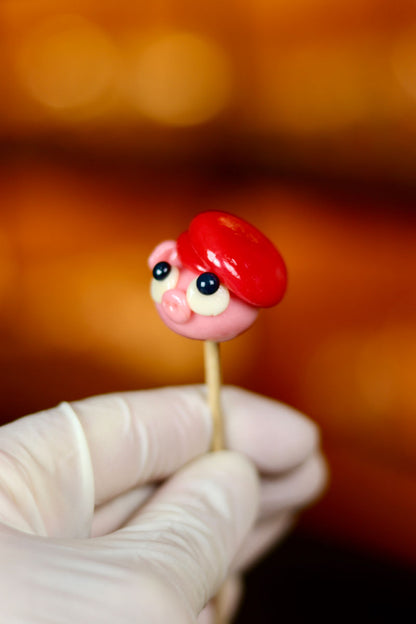 Une sucette sculptée en forme de cochon portant un béret rouge à la fraise. Photo prise dans notre boutique magique

