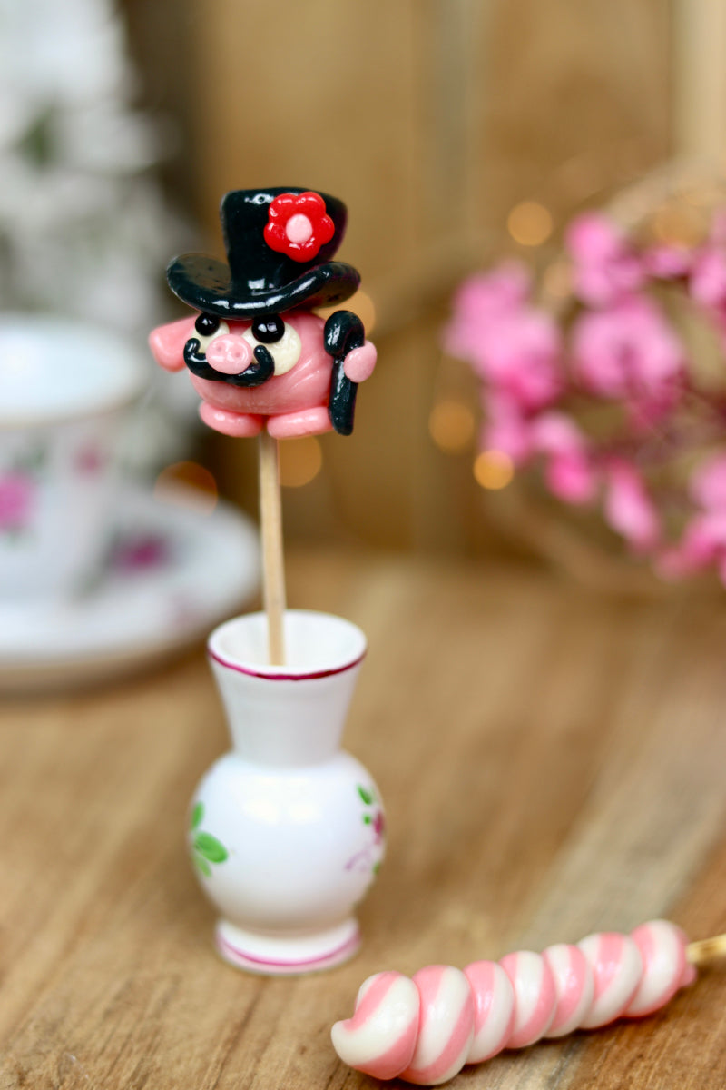 sucette sculptée en forme de cochon à la fraise habillé d'un chapeau au cassis. 