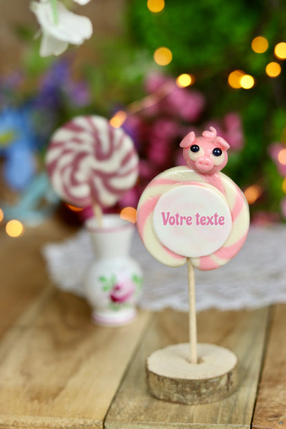 Sucette imprimée à personnaliser de votre texte, à la vanille et à la fraise avec un cochon sculptée en sucre cuit dessus. Dans un décor féérique