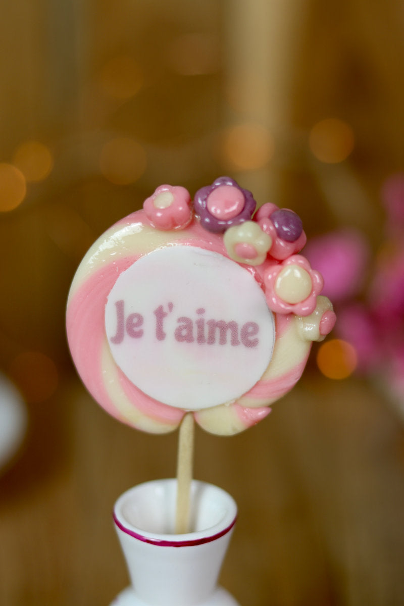 sucette en forme de spirale écrit je t'aime au centre, avec des petites fleurs dessus