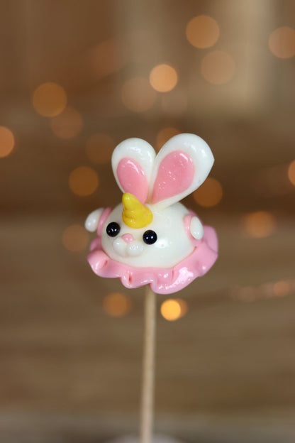 Une sucette sculptée en sucre cuit. Elle est en forme de lapin à la banane, qui porte une petite robe rose à la fraise et une corne sur le front