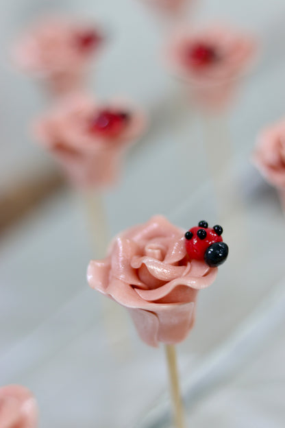 Sucette sculptée en forme de rose à la framboise avec une coccinelle dessus. Photo prise dans l'atelier